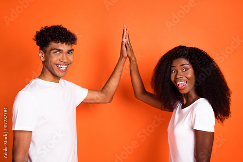 Photo of young happy excited smiling positive afro best friends clap hands high five isolated on orange color background