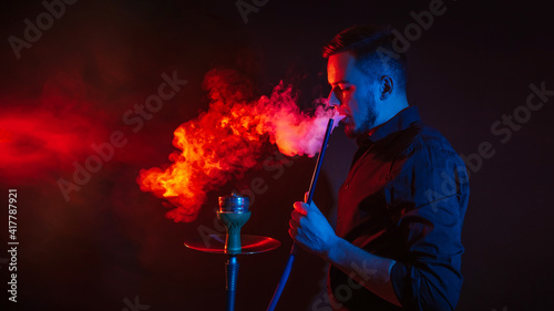 man is smoking a hookah in bar and blowing a cloud of smoke