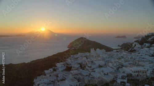 Aerial Pan of White Houses in Plaka Village and Sun Setting Behind Mountain photo