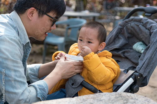 An Asian father takes his son to the park to share food