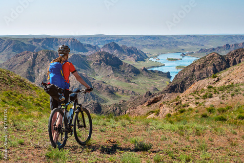A traveler guy on a bicycle looks out over a beautiful river valley. A beautiful natural landscape of a river valley with hills and flowering meadows