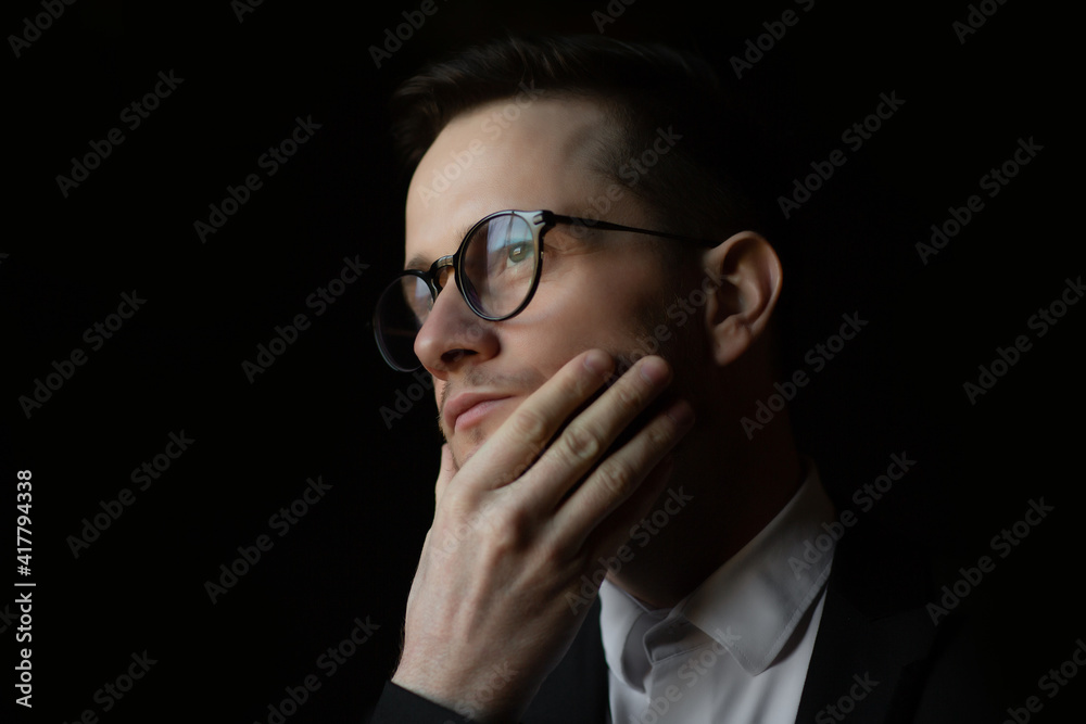 Close-up of businessman in suit and eyeglasses over dark black background. Close-up of businessman in suit and eyeglasses over dark black background.