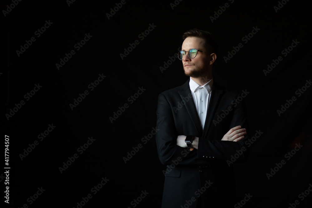 Portrait of a successful young and confident businessman with his hands folded on a dark black background. Portrait of a successful young and confident businessman with his hands folded on a dark black background.