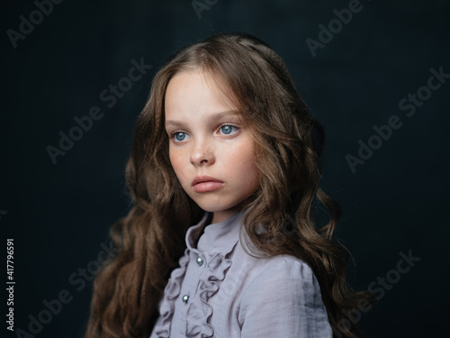portrait of a beautiful girl in a gray dress on a dark background and curly hair blue eyes