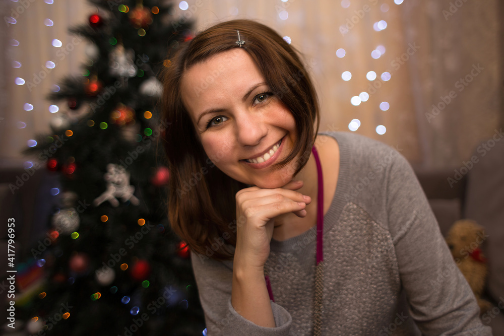 Portrait of a smiling woman at christmas time. Blurred decorated Christmas tree and glowing garland on the background. Portrait of a smiling woman at christmas time. Blurred decorated Christmas tree and glowing garland on the background.