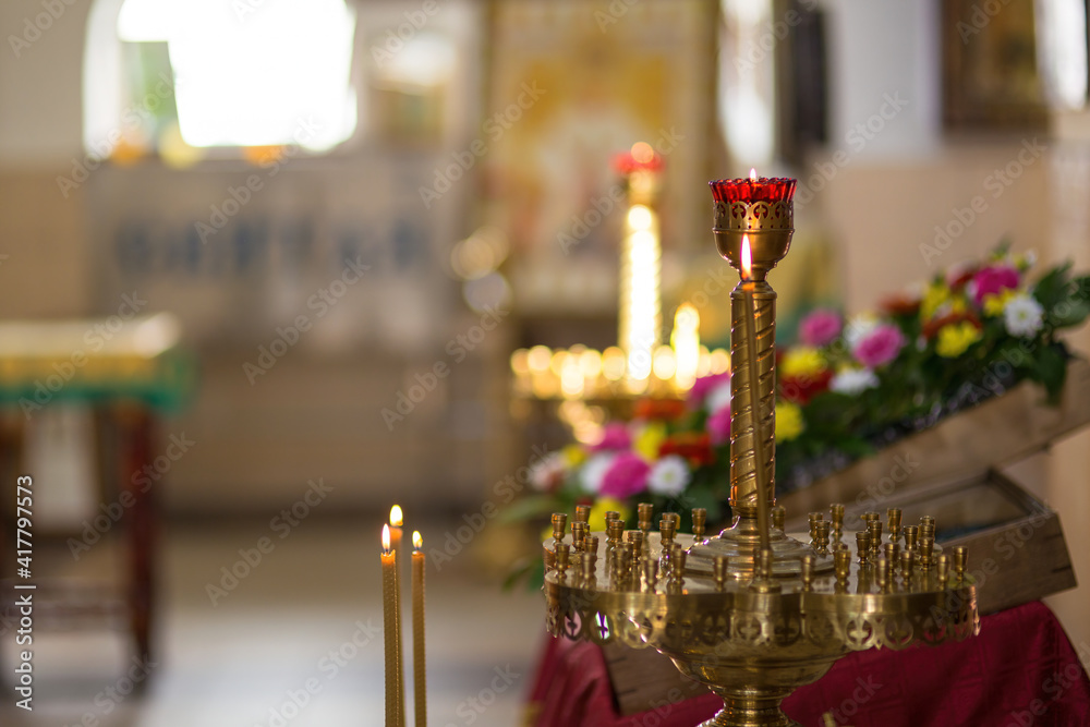 Naklejka premium Beautiful brass candlestick with burning candles in a Christian church. Colorful blurred background