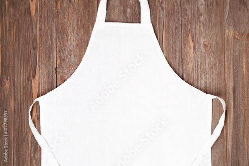 Blank white apron template on wooden background, copy space. Kitchen, cooking clothing mockup