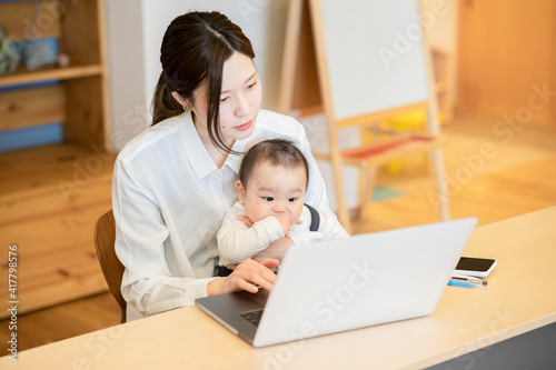 赤ちゃんを抱えてノートパソコンを操作する女性