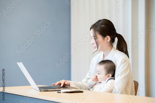 赤ちゃんを抱えてノートパソコンを操作する女性