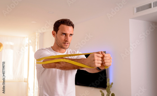 side view of sporty man doing chest workout with elastic resistance bands at home