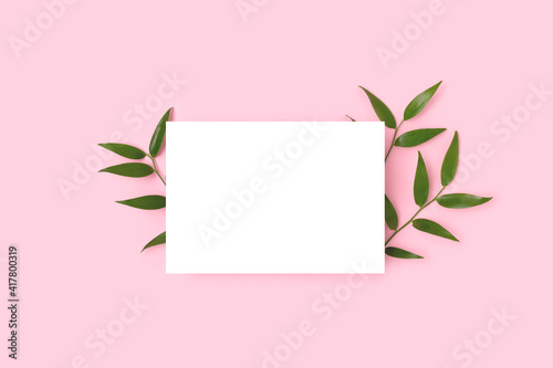 Empty paper card mockup and green leaves of pistachio on a pink background. Summer composition with copyspace.