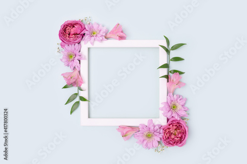 Empty flower frame made of rose, aster and alstroemeria on a blue pastel background. Greeting card template with copyspace. Floral layout.