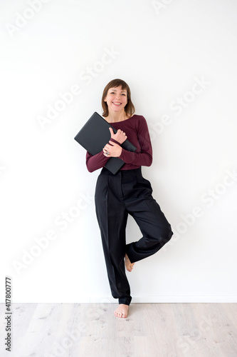 Woman with a laptop barefoot in full growth stands against a white wall