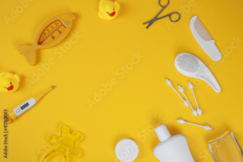 Baby accessories for bathing on yellow background, flat lay. Composition with baby accessories and space for text. Baby cotton swabs, cream, thermometer, ducks, combs, scissors, teething