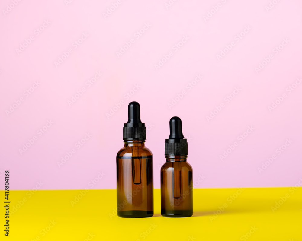 Two brown glass cosmetic oils pink and yellow background