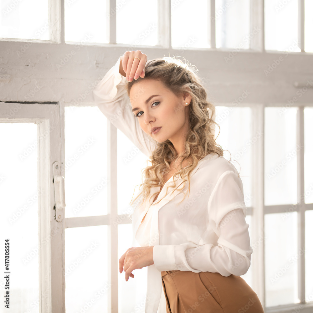 Portrait of a gentle blonde girl in a white business blouse on the background of a wooden window Portrait of a gentle blonde girl in a white business blouse on the background of a wooden window