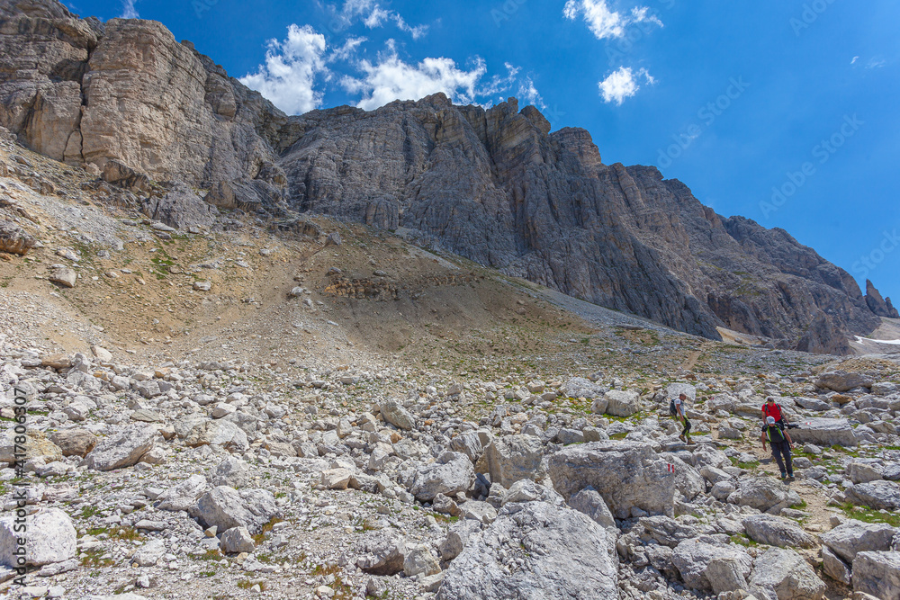 Unrecognizable trekkers walking on a hiking trail at the foots of western rocky wall of the mount Settsass, Dolomites, Italy