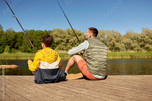 family, generation, summer holidays and people concept - father and son with fishing rods on river berth