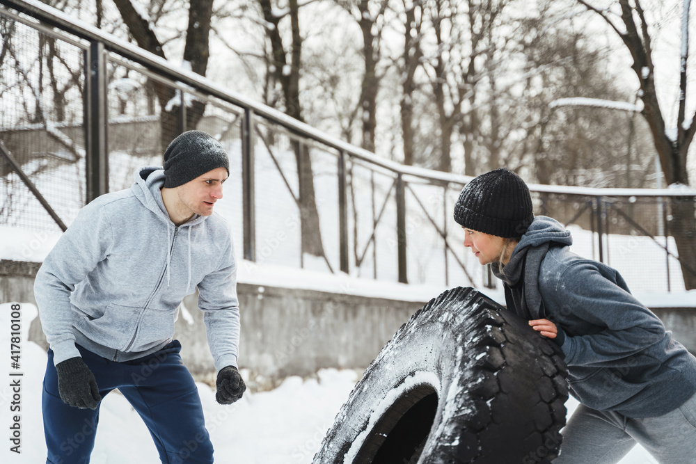 Trainer and his woman client during workout with a tire during cold winter and snowy day