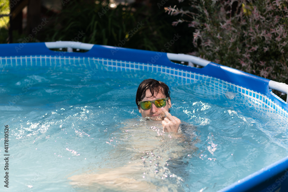 Man in glasses in the summer in a pool showing middle finger, fuck you, provocation and rude attitude.