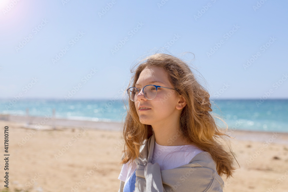 Closeup portrait of a beautiful young Caucasian fashion model posing on the seashore in sunny weather, looking into the distance, copy space