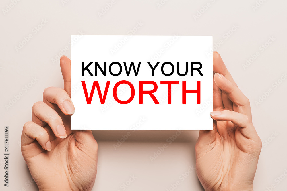 Female hands hold card paper with text KNOW YOUR WORTH on a yellow background. Business and finance concept Female hands hold card paper with text KNOW YOUR WORTH on a yellow background. Business and finance concept