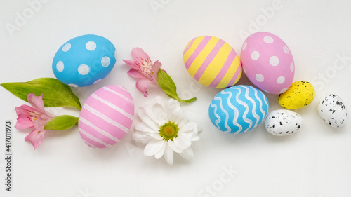 Happy Easter. Holiday composition. Handmade natural decoration. Pastel color pink blue yellow painted eggs with minimal design Spring flowers arrangement isolated on white background.