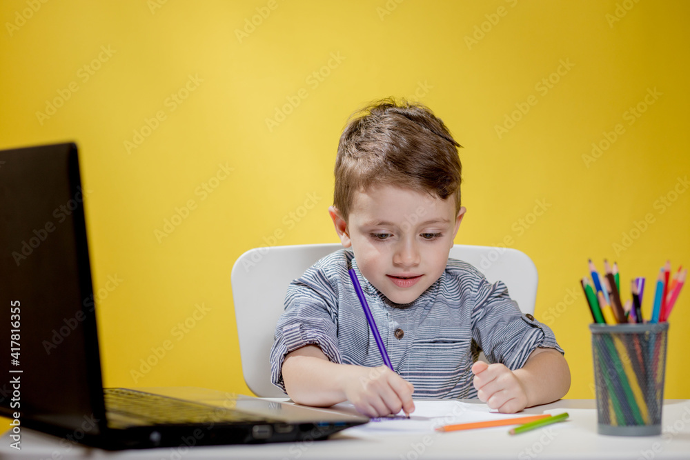 Happy Child using digital laptop doing homework on yellow background. Social Distancing, E-learning online education Happy Child using digital laptop doing homework on yellow background. Social Distancing, E-learning online education