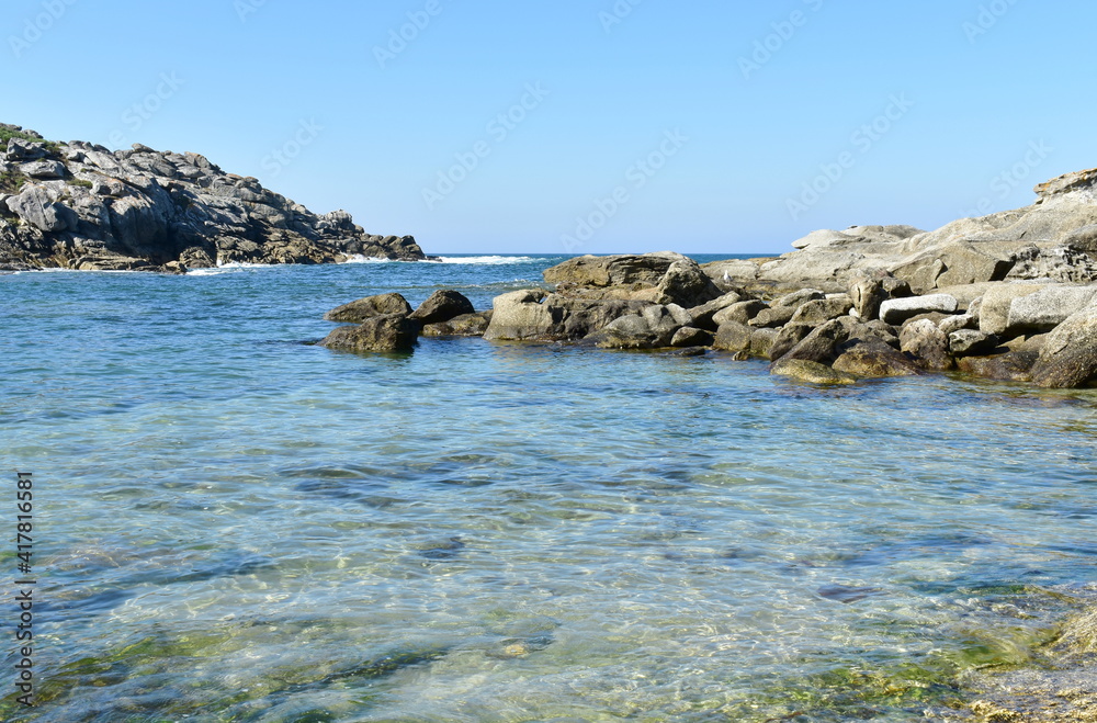 Beach with rocks, transparent water and blue sky at Rias Baixas Region. Galicia, Spain.