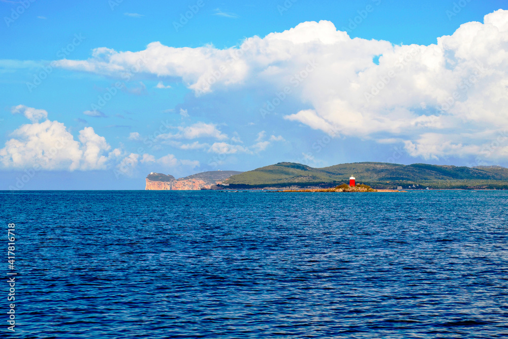 Piccolo faro su isoletta in mezzo al mare con promontorio di Capo Caccia all'orizzonte - Sardegna, Italia