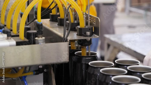 Empty beer cans are filled with fruit beer at the brewery's filling line. Close up.