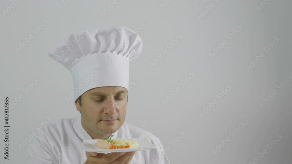 the chef smells the plate, white cap and uniform, smiling face the chef smells the plate, white cap and uniform, smiling face
