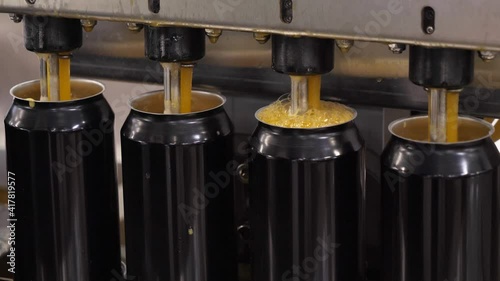 Empty beer cans are filled with fruit beer at the brewery's filling line. Close up.