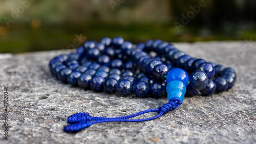 Blue buddhist mala prayer beads (lapislazuli) on stone, close up. Mindfulness and japa meditation accessory. photo