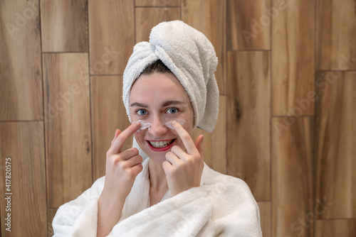 Pretty attractive girl wearing towel on head standing front of mirror in home bathroom. Daily hygiene and skincare