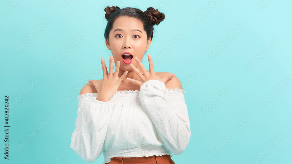Close-up portrait of amused, surprised asian girl receive incredible good news, touch cheeks and smiling amused, glad to win, triumphing, blue background