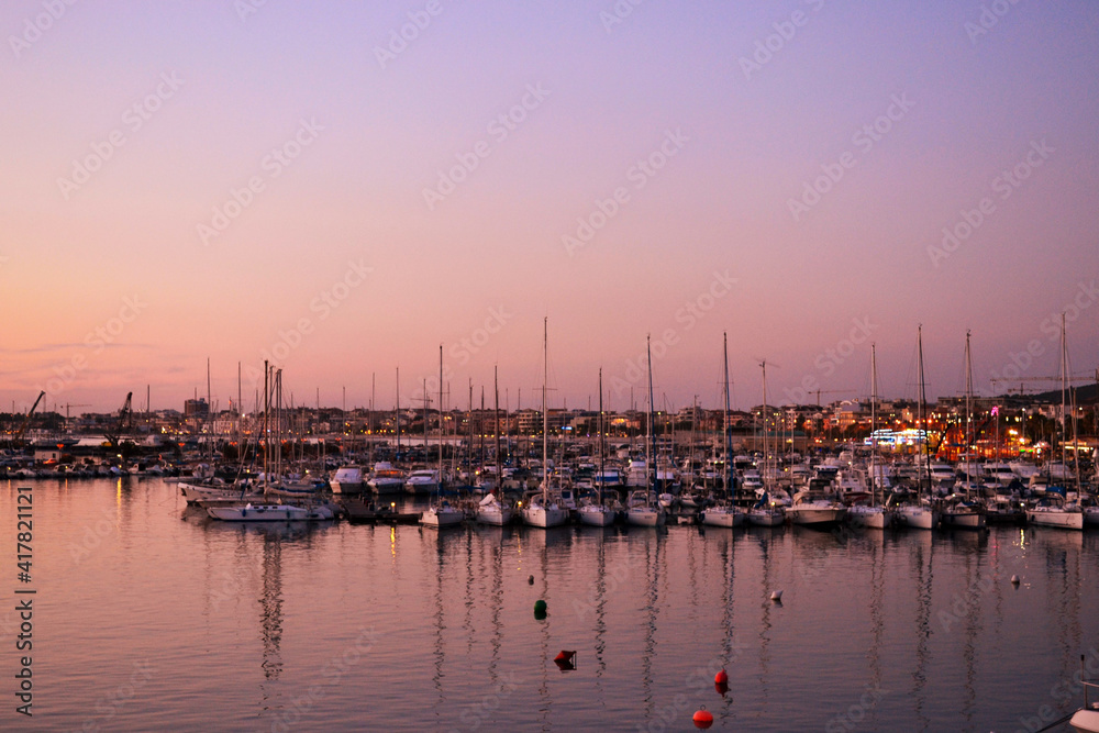 Cielo e mare rosa appena prima del tramonto con barche vela attraccate al porto