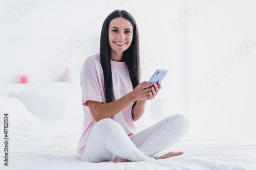 Photo of sweet adorable young lady sleepwear sitting bed smiling reading modern device indoors room home