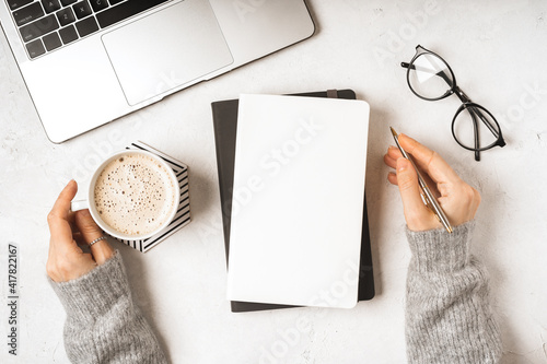 Top view woman hands with blank paper Notebook, leaf, laptop keyboard, cup of coffee, glasses and pen. Desktop mock up, Flat lay of white working table background with office equipment, mockup.
