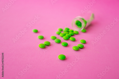 a glass ampoule is lying on the table a pile of green pills close up on a pink background