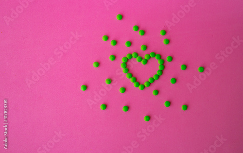 heart of green pills on a pink background  heart-shaped pills laid out on a table close-up