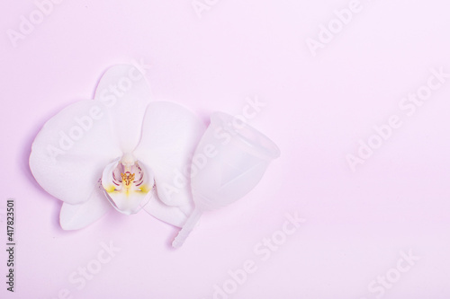 Eco-friendly siliconemenstrual cup with orchid on pink background.