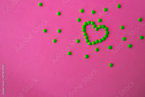 heart of green pills on a pink background, heart-shaped pills laid out on a table close-up