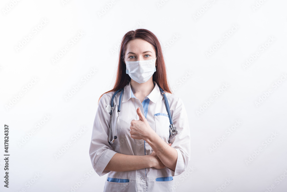 Portrait of a female doctor in a white uniform who shows an approving gesture thumb up in the studio on a white background Portrait of a female doctor in a white uniform who shows an approving gesture thumb up in the studio on a white background