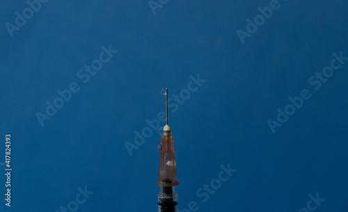 The needle of a syringe with a vaccine close-up on a blue background