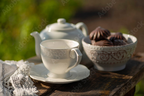 Elegant cup  lace tablecloth  teapot  marshmallow in chocolate  wooden table. Outdoor breakfast  picnic  brunch  spring mood. Soft focus