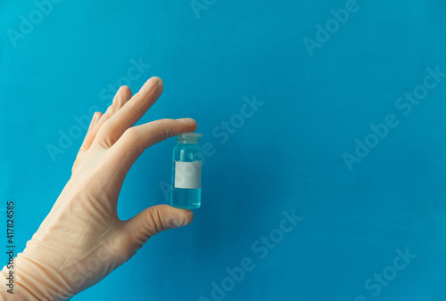 a hand in a white protective medical glove holds the vials of the vaccine close up on a blue background