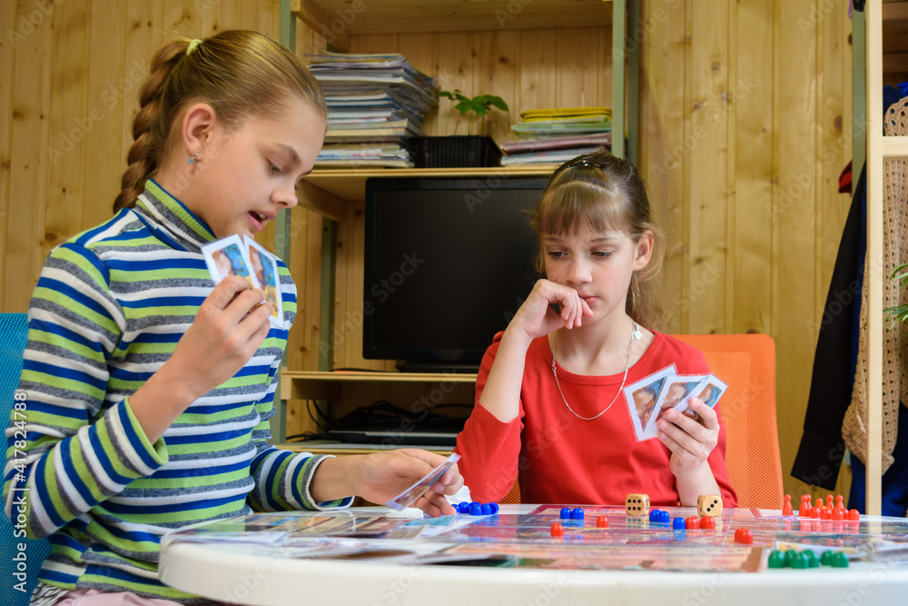 Fototapeta premium A girl plays a card from her hand, another girl looks thoughtfully