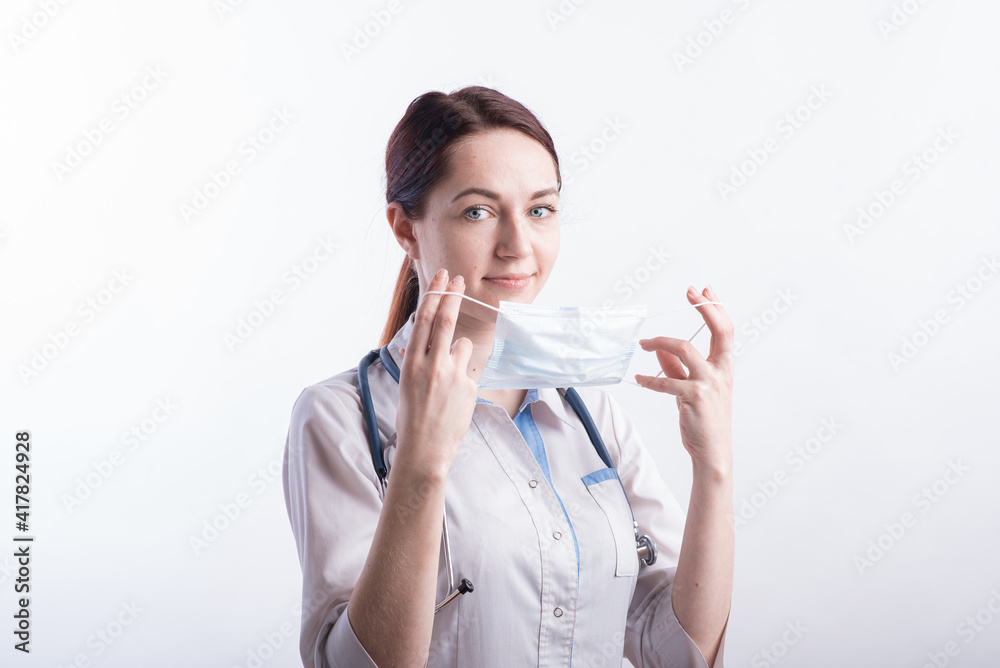 Portrait of a female doctor in a white uniform who puts on a medical mask in the studio on a white background Portrait of a female doctor in a white uniform who puts on a medical mask in the studio on a white background