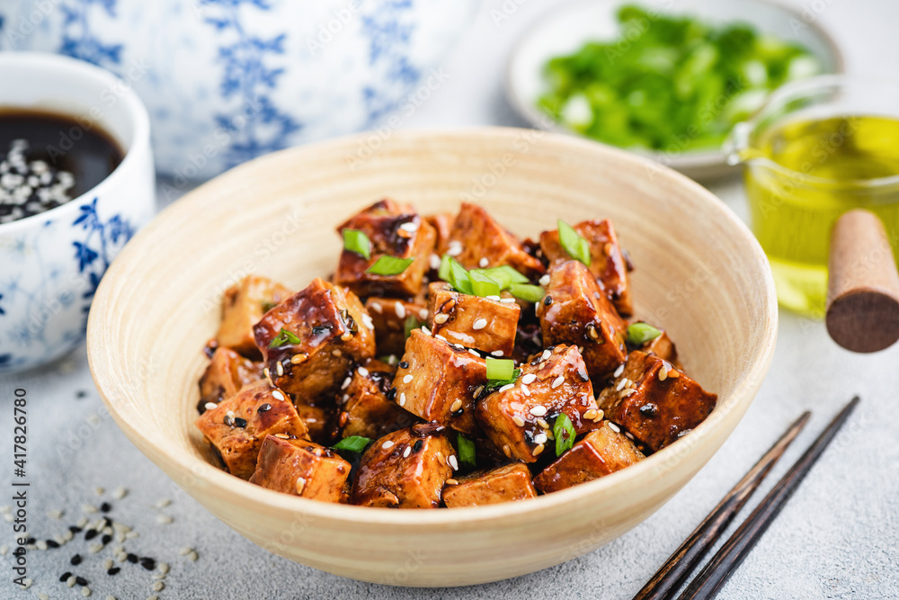 Vegan fried teriyaki tofu with scallions and sesame seeds in bamboo bowl. Asian cuisine food